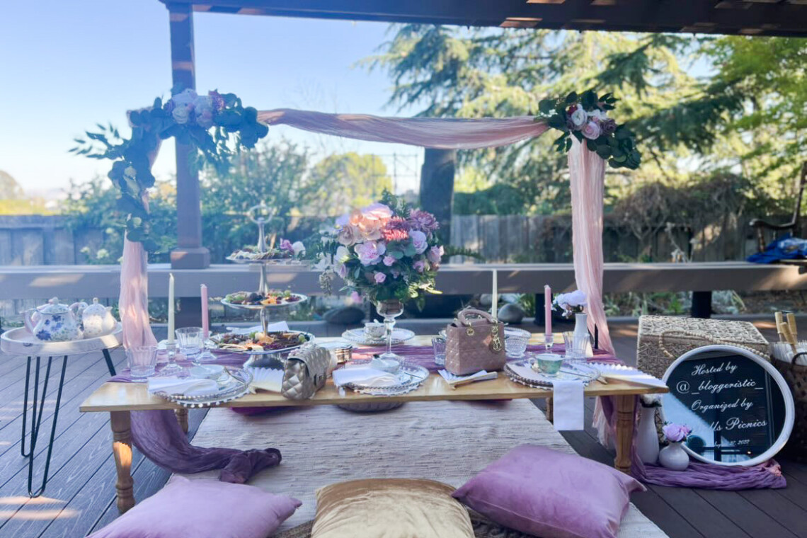 Gold and mauve colored picnic set up with large floral bouquet, purses, and teapots as decorations.