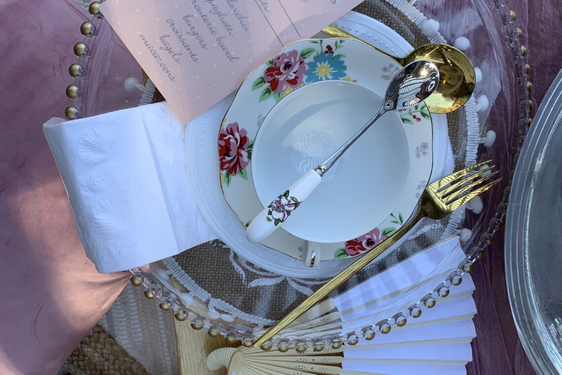 Table setting of a luxury picnic with cute menu, floral plates, and a white fan.