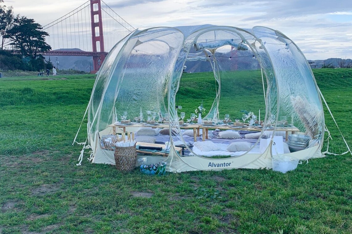 A picnic set up inside a bubble tent and overlooking the Golden Gate Bridge.