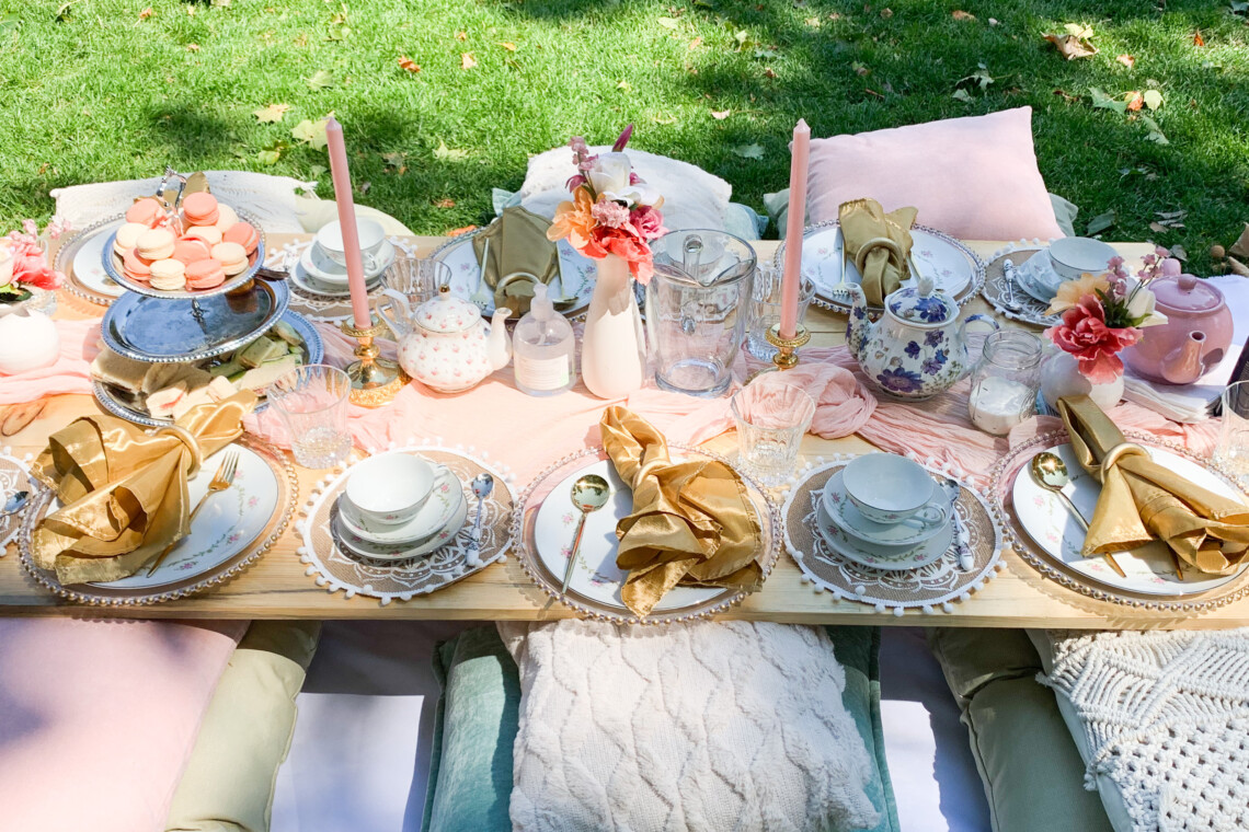 Pink picnic set up with macaron platter, teapots, golden napkins, and boho pillows.